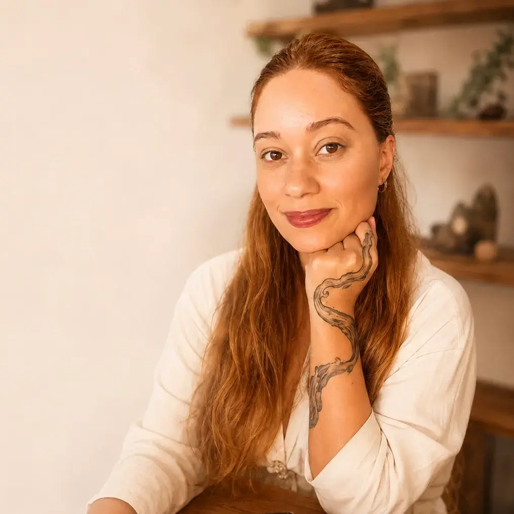 Retrato de Aline Antunes, de cabelos ruivos e blusa de linho clara, apoiando o queixo na mão
